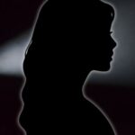 black silhouette of woman against a black backdrop with flashlight shining