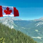 canadian flag flying against backdrop of forested mountains