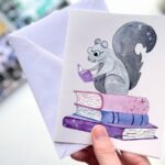 a greeting card with an illustration of a squirrel on a stack of books reading