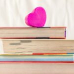 stack of books with the edges facing forward and a pink paper heart resting on top
