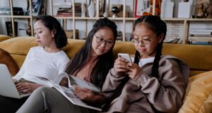 young Asian girls and one woman sitting together reading and talking on a couch