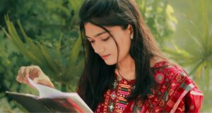 a young, fair-skinned Asian woman in brilliant red traditional clothing reading a book outside