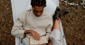 brown-skinned Black man with cornrows reading in a hammock beside someone with fair skin