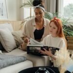 a Black and a white woman sit together and look at a book