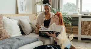 a Black and a white woman sit together and look at a book