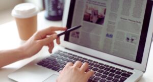 a light-skinned hand pointing at news article displayed on laptop