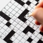 a hand filling out a crossword puzzle in pencil