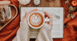 someone holding a latte with an open book and decorative pumpkins