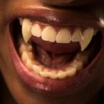 open mouth of a brow-skinned person with red lips and vampire fangs