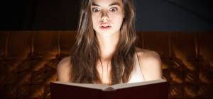 Gorgeous shocked looking young brunette woman reading book in creative lighting.