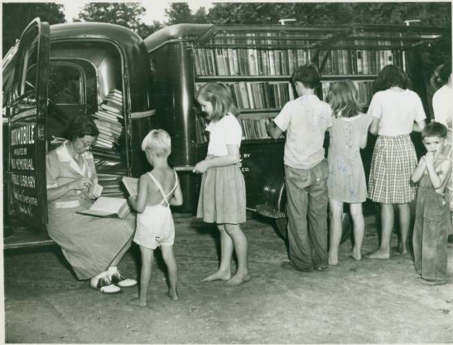 children line up in front of a bookmobile, browsing and checking out books