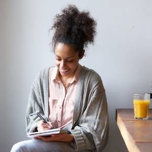 Portrait of a smiling woman writing on note pad at home