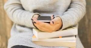 girl sitting with a cell phone and books