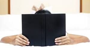 Unrecognizable Woman reading a book on bed