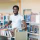 Portrait of young male librarian with trolley of books in library