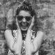 black and white photo of a girl laughing, holding her ears, wearing sunglasses