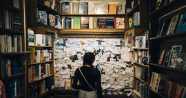 A person looks at a cork board covered in sticky notes in a bookstore.