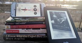 Stack of books by African-American authors listed in the article. One is on a kindle leaning against the stack, and another is an audiobook on a phone screen set on top of the stack.