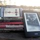 Stack of books by African-American authors listed in the article. One is on a kindle leaning against the stack, and another is an audiobook on a phone screen set on top of the stack.