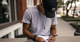 Man writing with left hand in a notebook on his lap