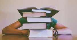 Person crouches behind a pile of books.