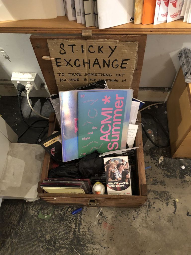 Wooden box chock-full of publications and CDs, with a sign reading "STICKY EXCHANGE"