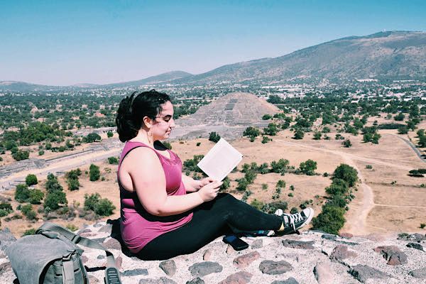 A woman sitting and reading a book with a pyramid in the background