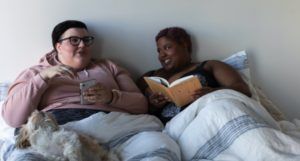 a photo of a queer couple reading in bed together