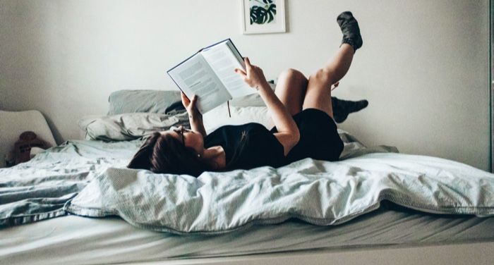 a photo of a person reading in bed, lying on their back and kicking their legs