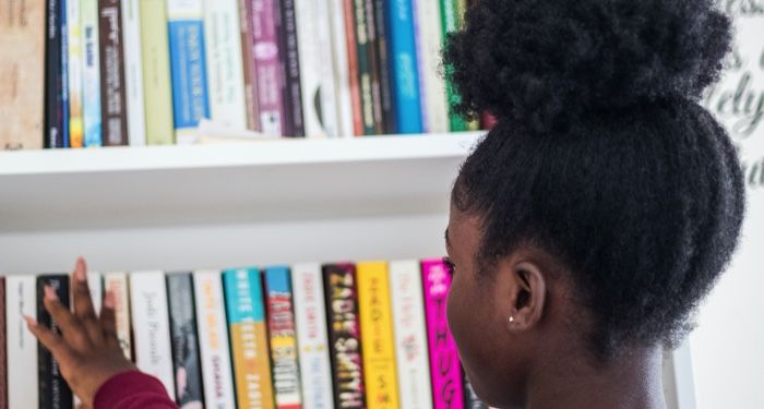 a photo of a Black teenager with their hair up browsing YA books