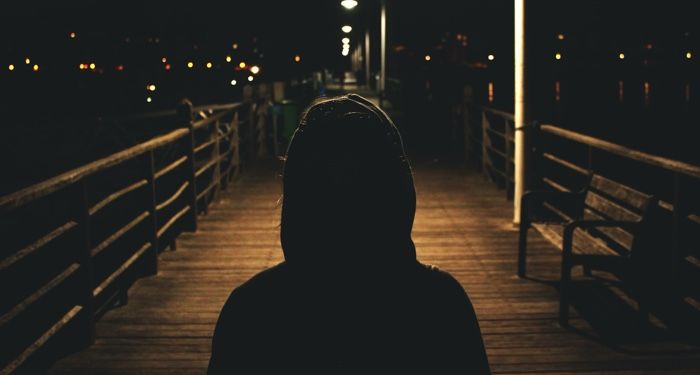 image of a person in a black hoodie on a dimly lit street at night