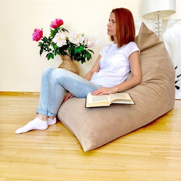 woman sitting with book in large tan triangle beanbag