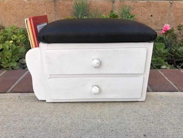 white stool with black cushion top featuring two drawers and side book holder