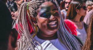 a photo of a Black woman at a Pride parade with shimmery rainbow face makeup