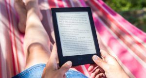 person in a striped hammock reading on an Amazon Kindle