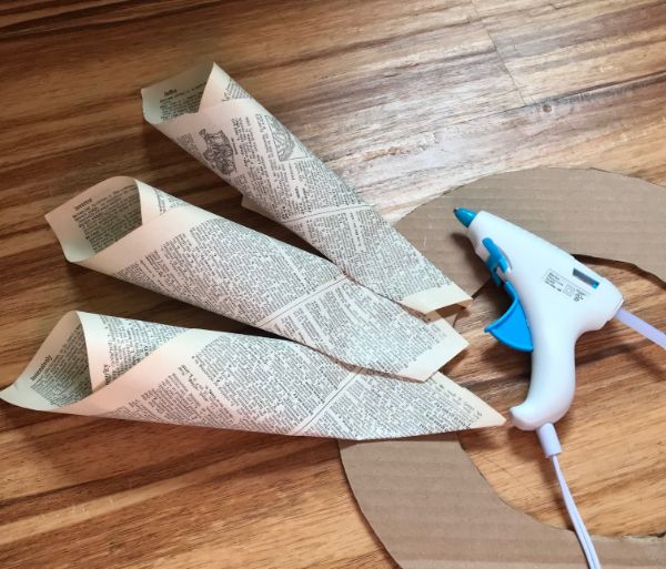 A picture of a glue gun and book page cones adhered to cardboard wreath