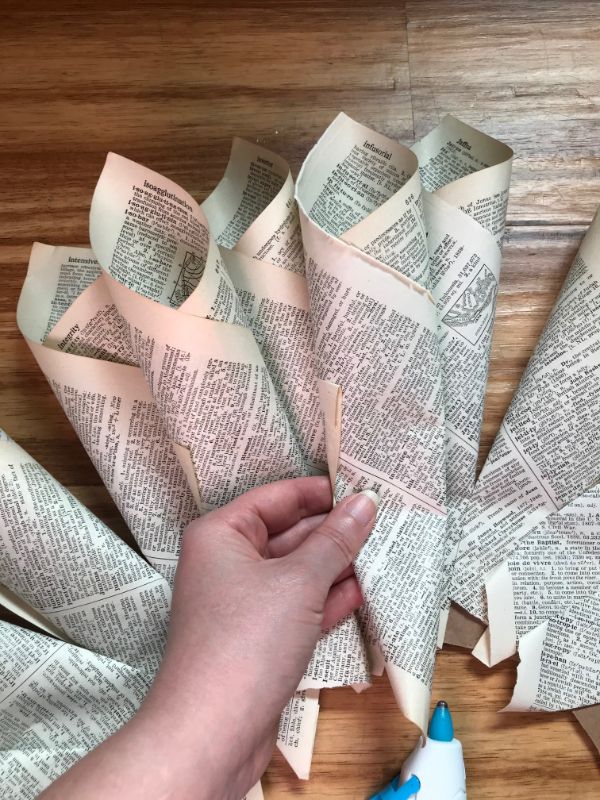 A picture of a hand placing a book page cone on a cardboard wreath  with a glue gun