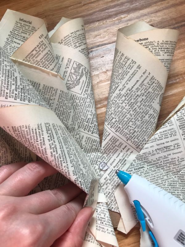 A picture of a hand placing a book page cone on a cardboard wreath with a small dot of hot glue
