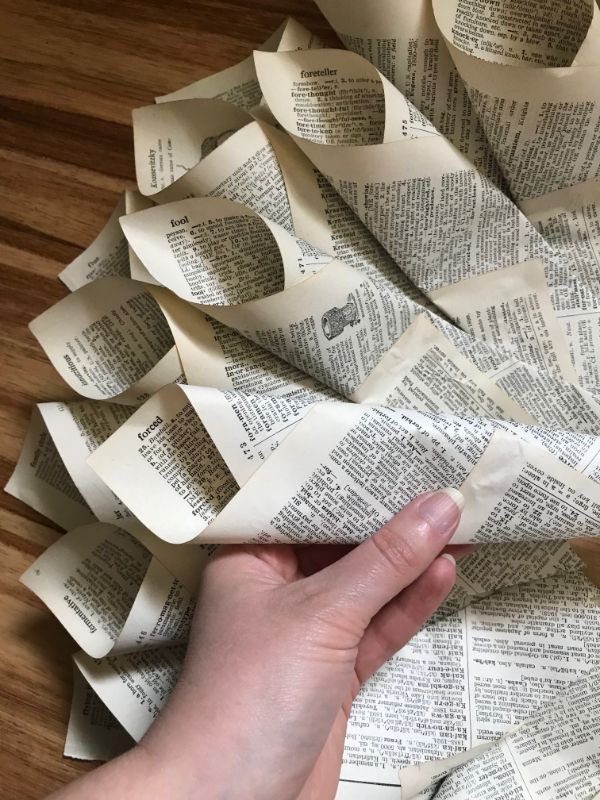 A picture of a hand placing a book page cone on a cardboard wreath