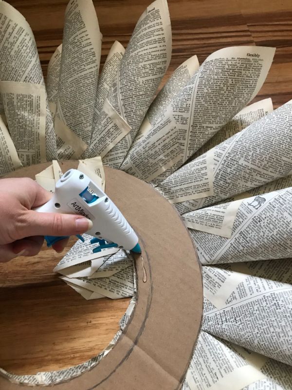 A picture of a hand hot gluing the back of a book page wreath 