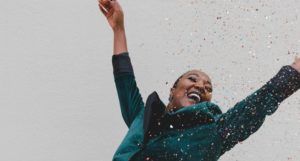 image of Black women in green jacket raising her hands with joy https://unsplash.com/photos/POzx_amnWJw