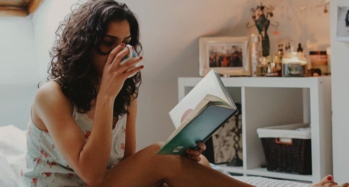 woman drinking tea relaxing and reading in bed