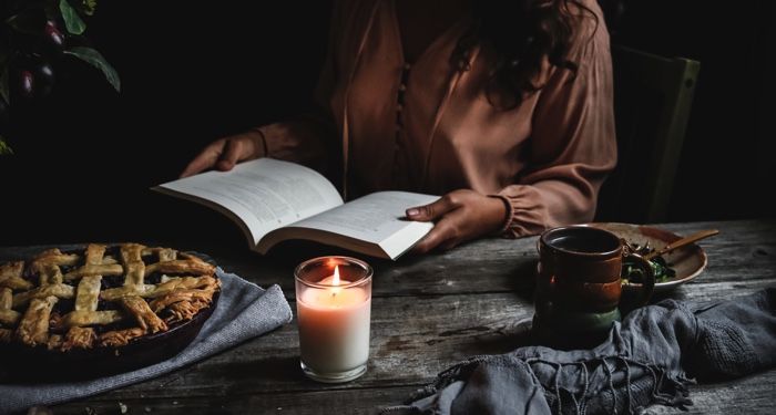 woman reading at a rustic table with pie and knitting