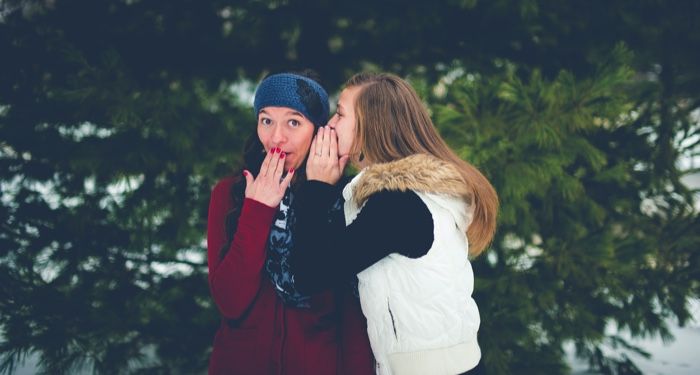 woman whispering a secret into another woman's ear