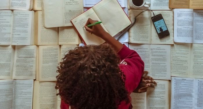 a photo of a woman writing on top of open books