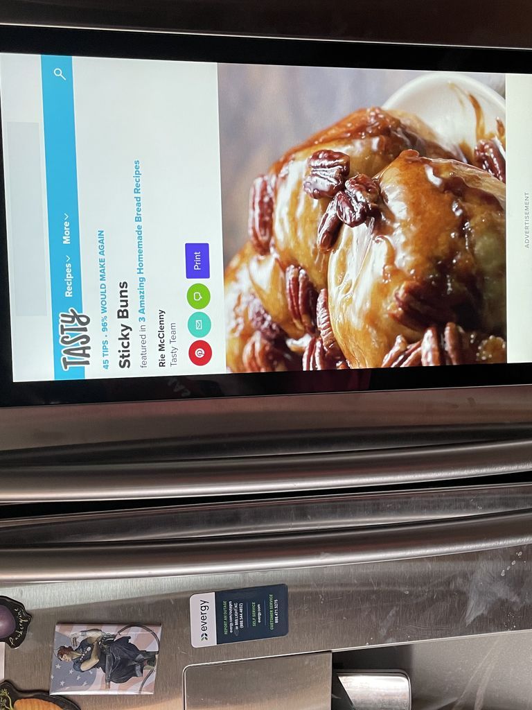 A digital screen showing a web page of a sticky buns recipe. The screen is attached to a fridge
