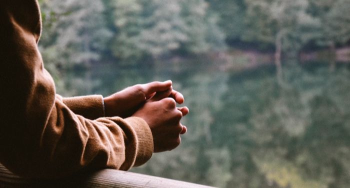 clasped hands on a railing in front of window overlooking lake and forest thinking