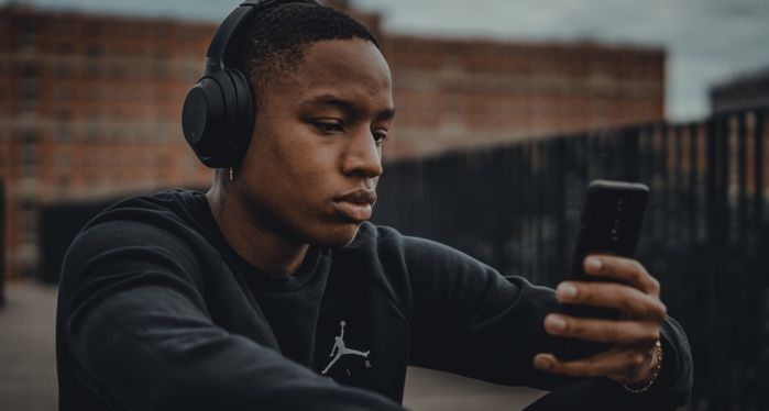 man wearing headphones and looking at cell phone outside