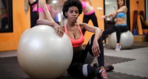 black woman sitting on floor with elbow on exercise ball in gym