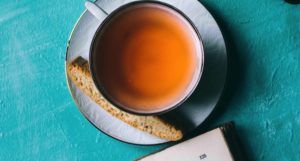 cup of tea with scone on serving plate against teal background with the corner of a book peeking at the bottom